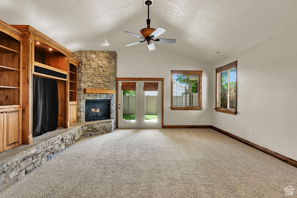 Unfurnished living room featuring a stone fireplace, a ceiling fan, carpet, and vaulted ceiling