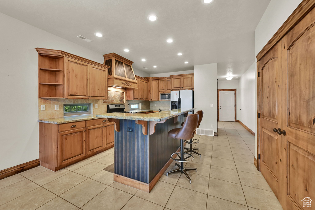 Kitchen with appliances with stainless steel finishes, recessed lighting, backsplash, premium range hood, and a breakfast bar area