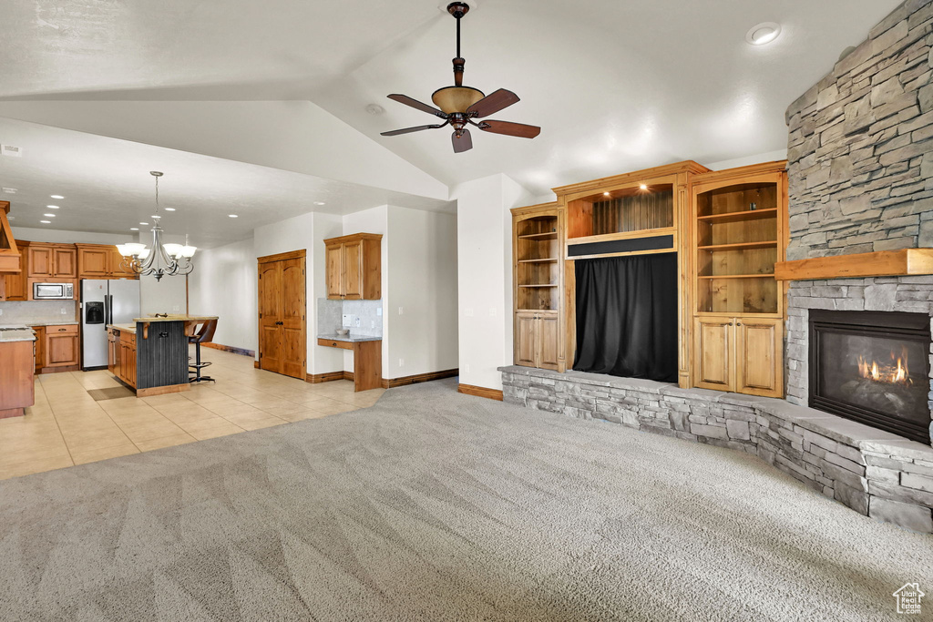 Unfurnished living room with light colored carpet, ceiling fan, lofted ceiling, light tile patterned flooring, and a stone fireplace