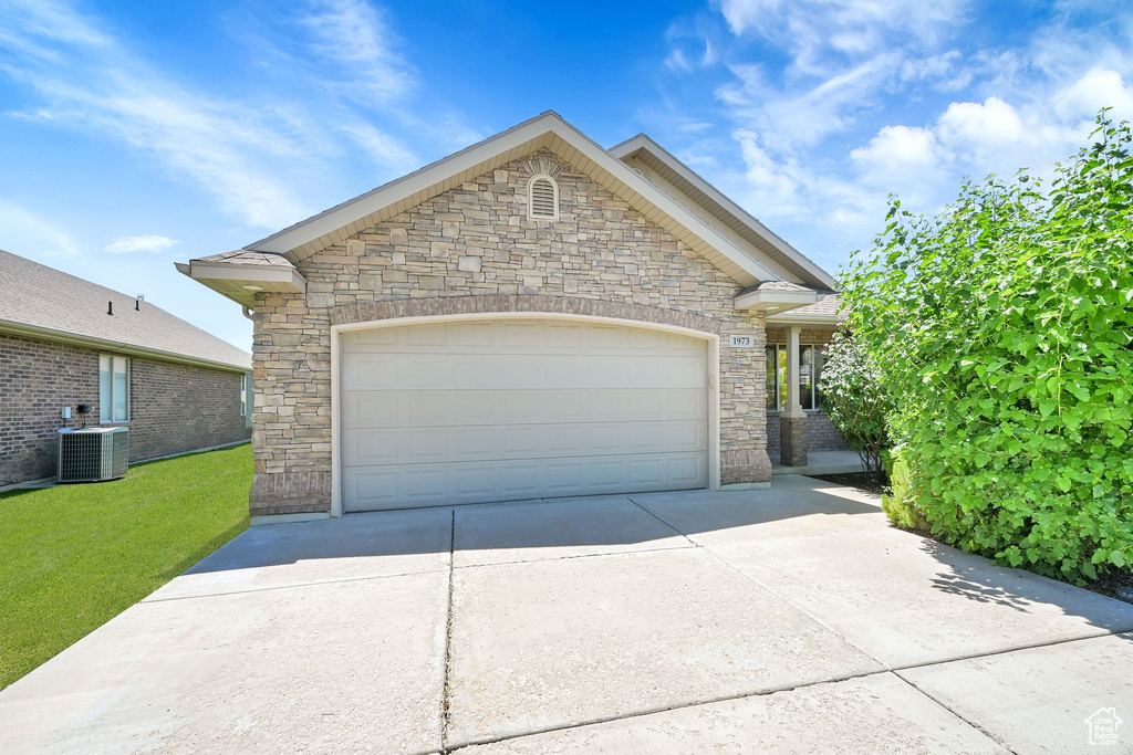 View of front of property featuring stone siding, concrete driveway, an attached garage, and a front lawn