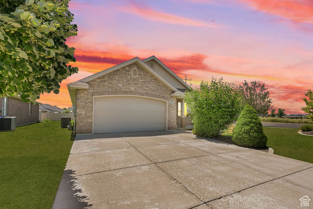 View of front of home with a yard, driveway, an attached garage, and stone siding