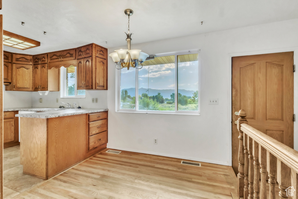 Kitchen with a chandelier, brown cabinetry, light countertops, light wood-type flooring, and pendant lighting