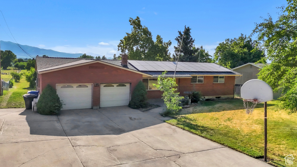Single story home featuring a front yard, concrete driveway, solar panels, a garage, and a mountain view