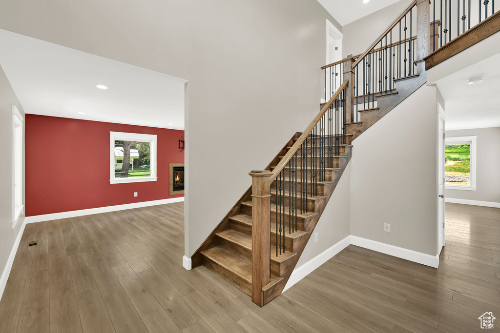 Stairs featuring wood finished floors, a glass covered fireplace, plenty of natural light, recessed lighting, and a towering ceiling