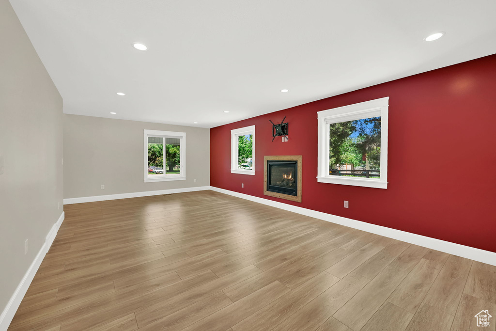 Empty room with light wood finished floors, recessed lighting, and a glass covered fireplace