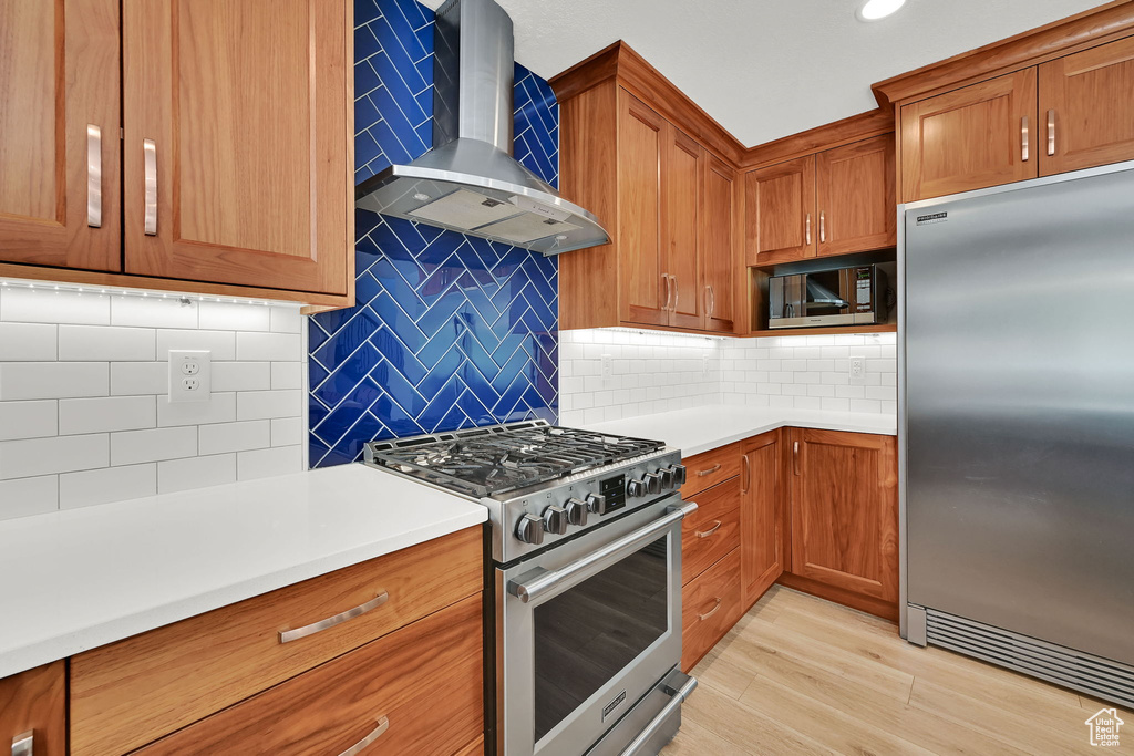 Kitchen featuring stainless steel appliances, wall chimney exhaust hood, decorative backsplash, brown cabinets, and recessed lighting