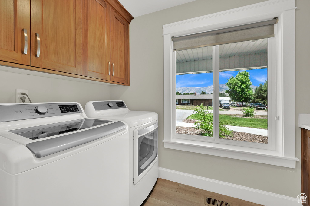 Laundry area with cabinet space, separate washer and dryer, and light wood-style flooring