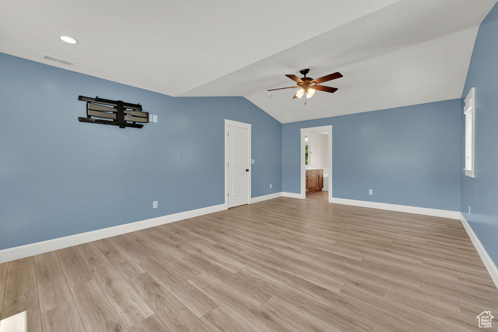 Empty room with ceiling fan, vaulted ceiling, and light wood-type flooring
