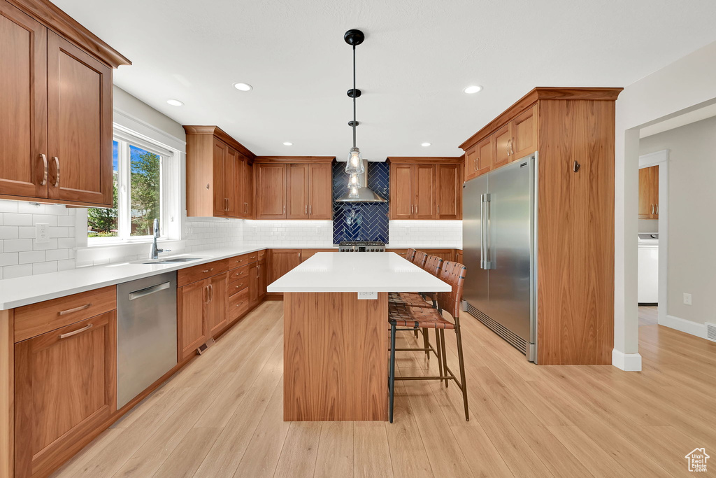 Kitchen featuring appliances with stainless steel finishes, wall chimney range hood, washer / dryer, a breakfast bar area, and light wood finished floors