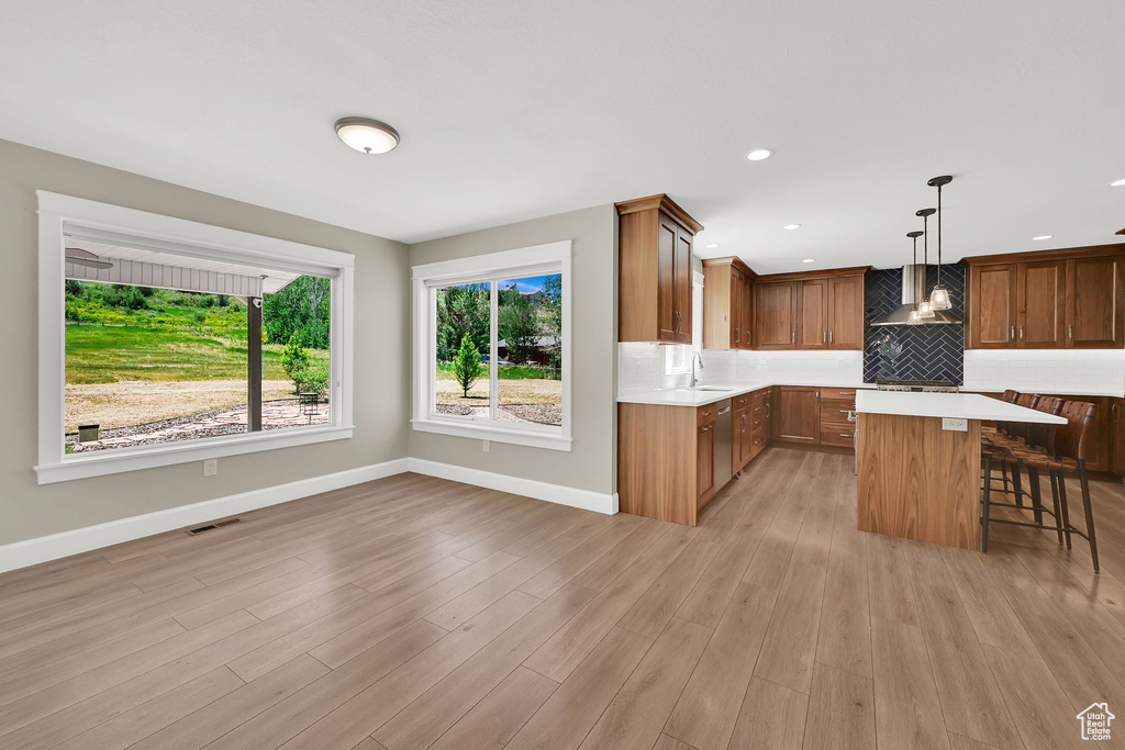 Kitchen featuring light countertops, a kitchen bar, stainless steel dishwasher, tasteful backsplash, and brown cabinets