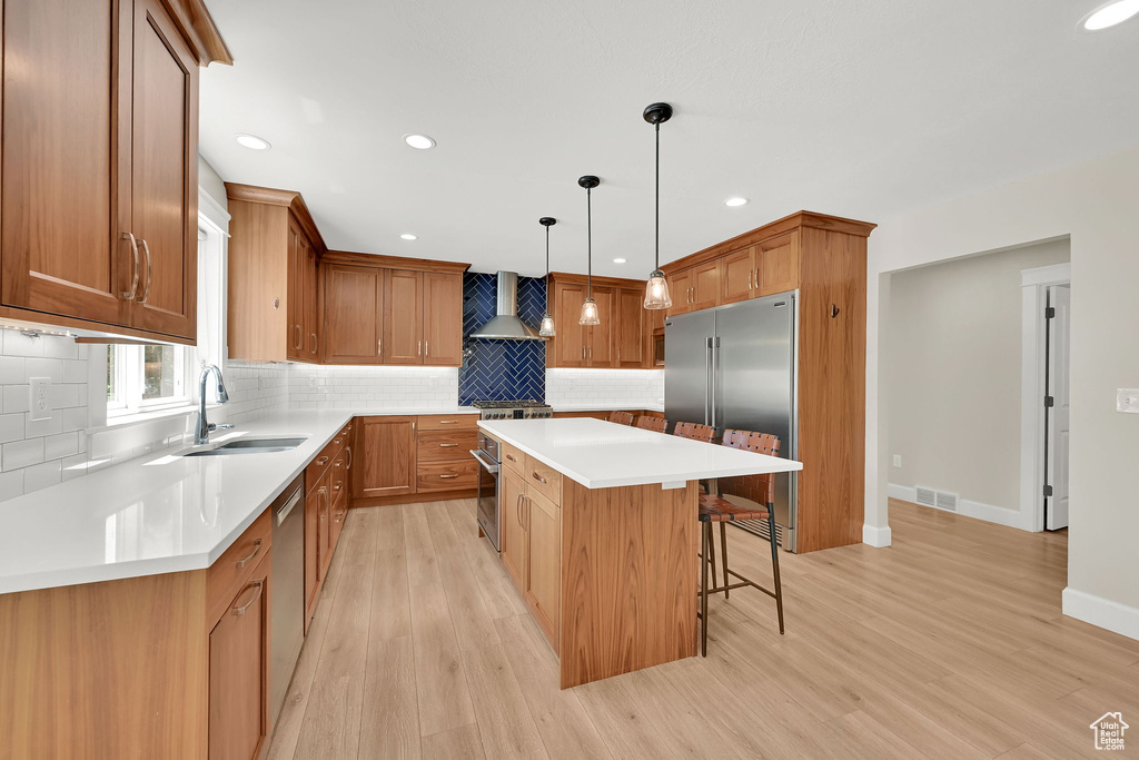 Kitchen featuring high end appliances, wall chimney exhaust hood, a center island, a kitchen bar, and decorative backsplash