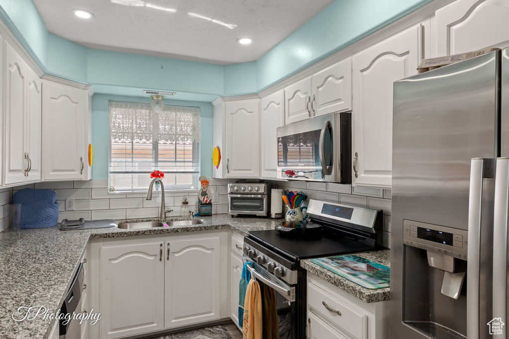 Kitchen featuring appliances with stainless steel finishes, white cabinetry, decorative backsplash, recessed lighting, and a textured ceiling