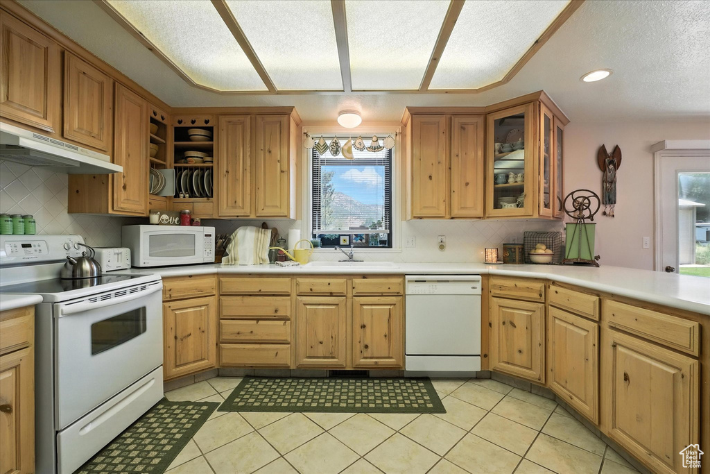 Kitchen featuring white appliances, under cabinet range hood, backsplash, light tile patterned flooring, and a textured ceiling
