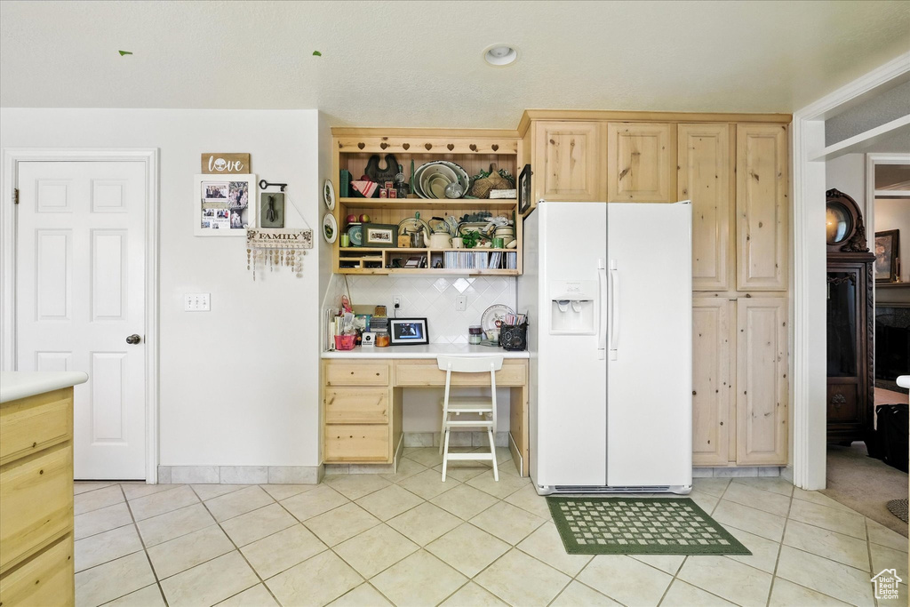 Kitchen featuring white fridge with ice dispenser, built in desk, light brown cabinets, and light tile patterned floors