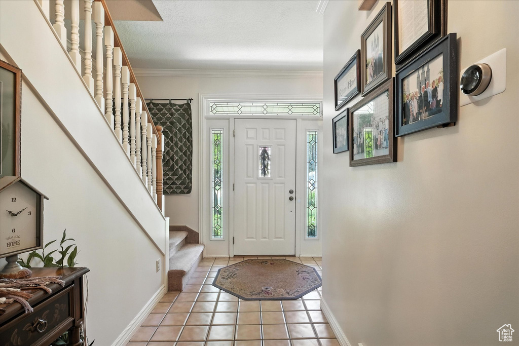 Foyer entrance featuring stairway, light tile patterned floors, and crown molding