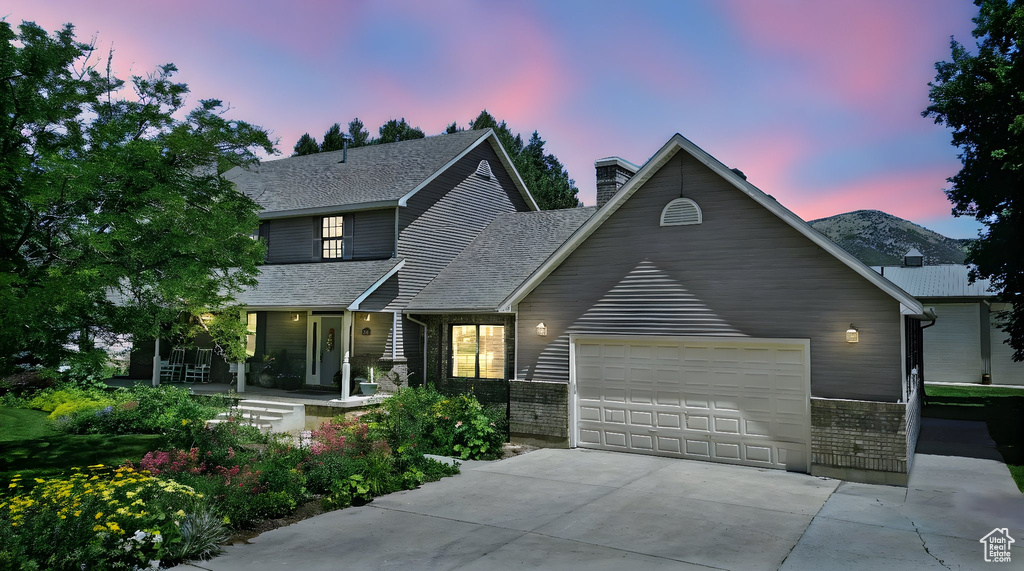 View of front facade with driveway, a porch, a garage, a chimney, and a shingled roof