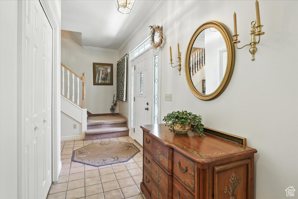 Foyer entrance with light tile patterned floors, stairs, and crown molding