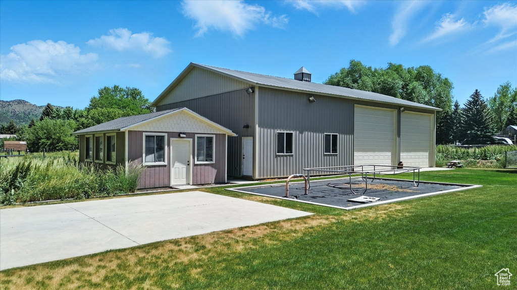 Rear view of house featuring an outdoor structure, a detached garage, a lawn, and a metal roof