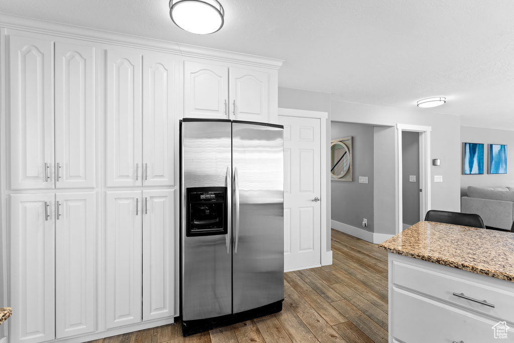 Kitchen featuring stainless steel refrigerator with ice dispenser, light wood-style flooring, white cabinets, and light stone countertops
