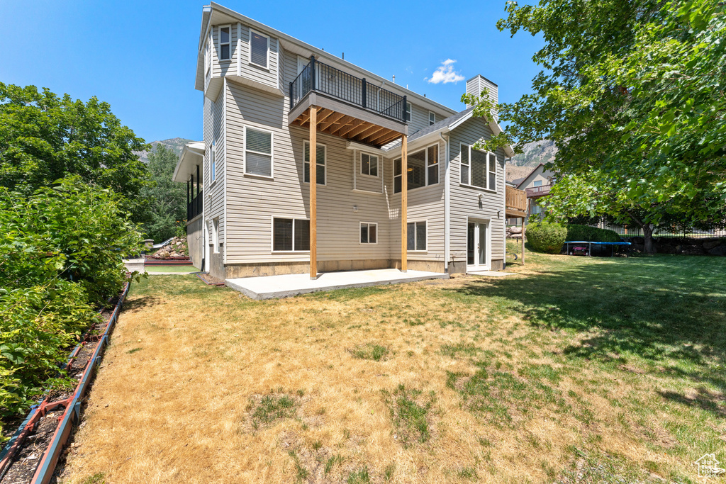 Rear view of property with a trampoline, a patio, a chimney, a yard, and a balcony