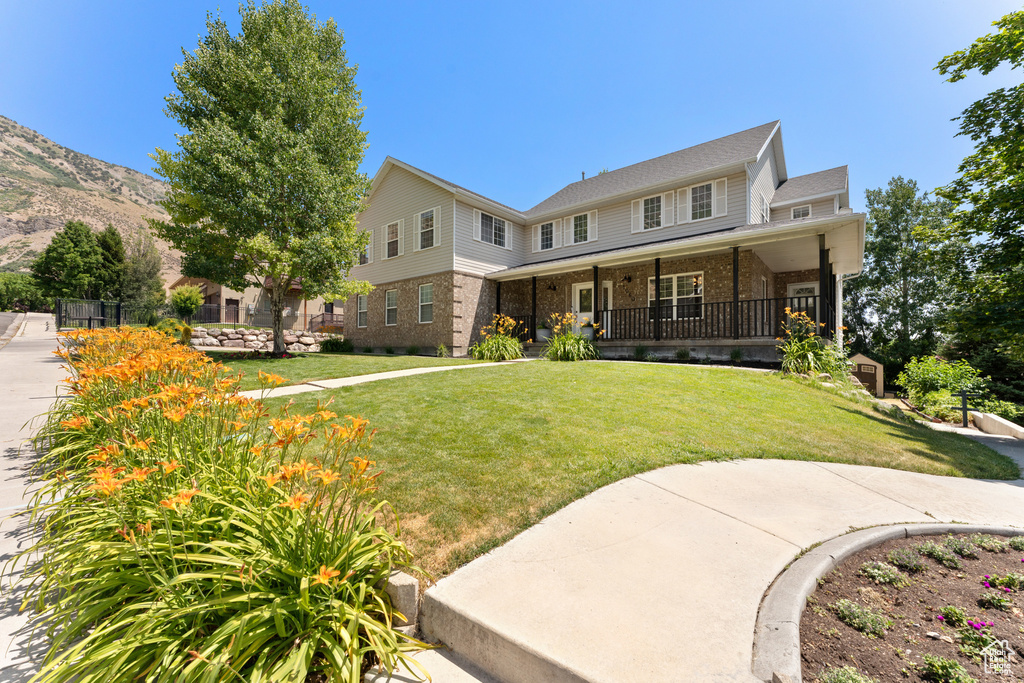 View of front of home with brick siding, covered porch, a front yard, and a mountain view