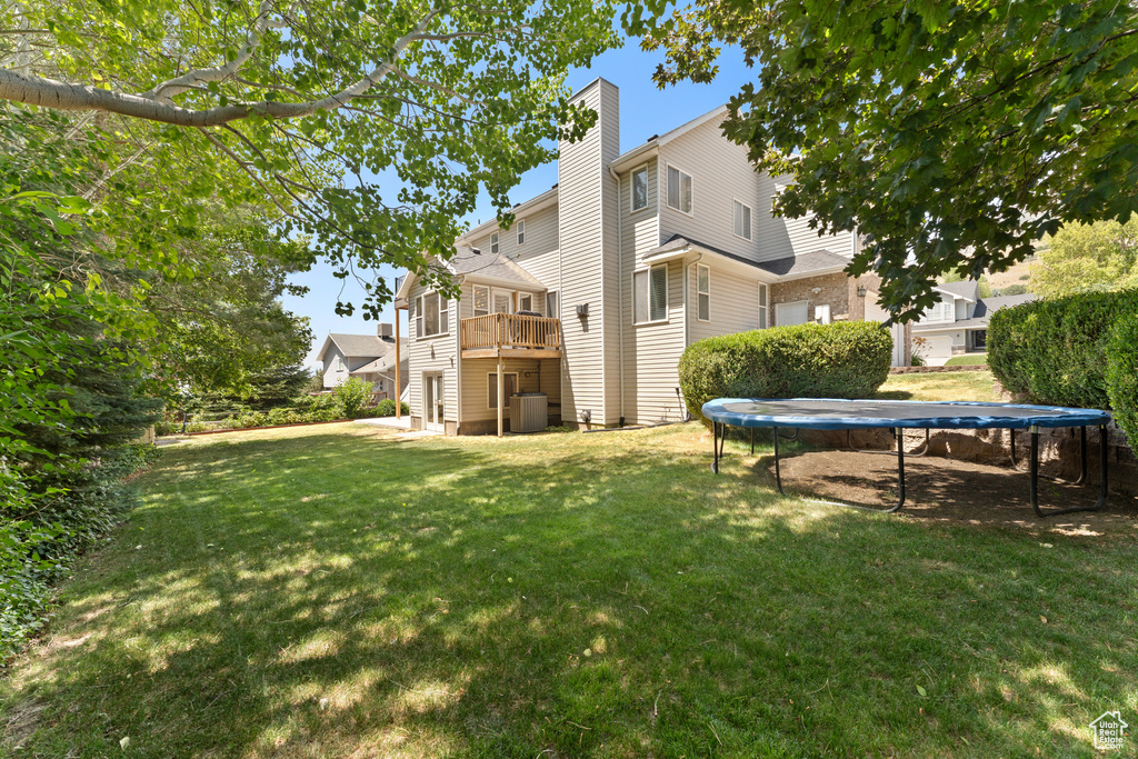 Back of house with a trampoline, a chimney, a lawn, and a deck