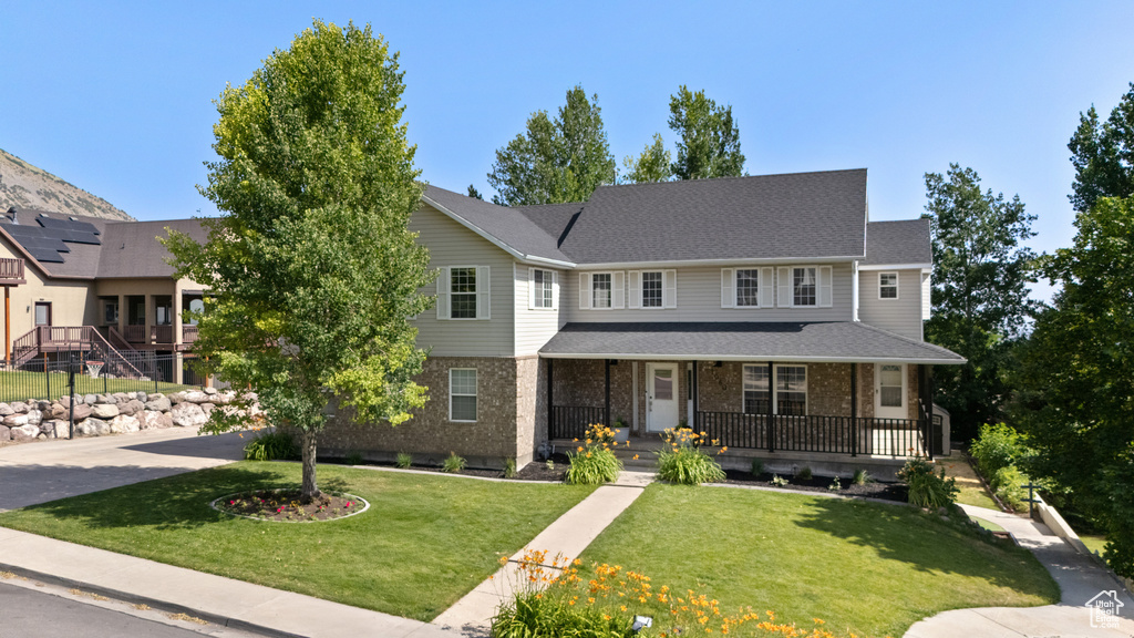 View of front of home featuring covered porch, a front lawn, and brick siding