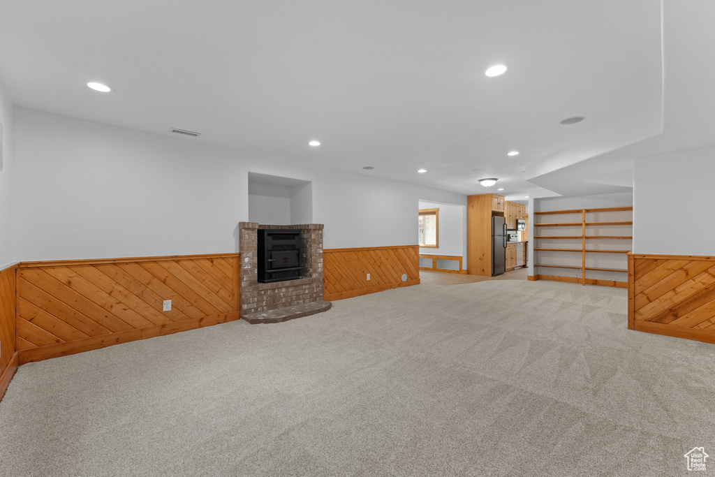 Basement with freestanding refrigerator, a wainscoted wall, wood walls, carpet, and a fireplace