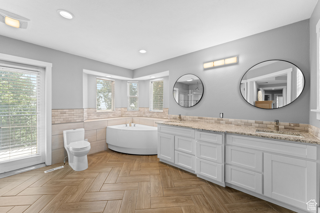Full bathroom featuring tile walls, double vanity, recessed lighting, a garden tub, and wainscoting