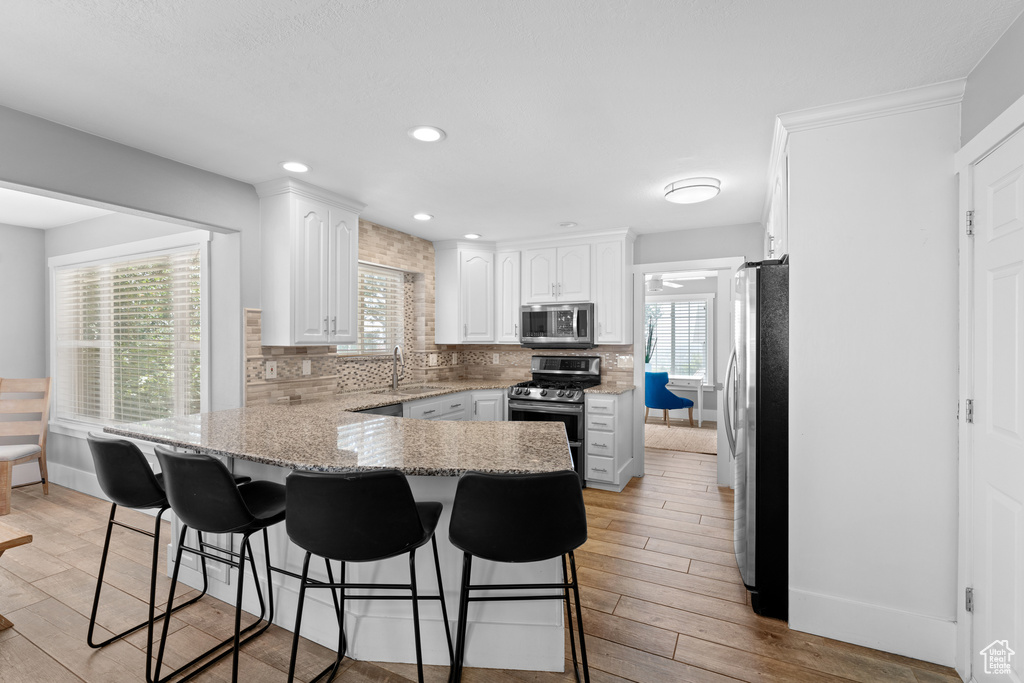 Kitchen featuring appliances with stainless steel finishes, a peninsula, white cabinets, a breakfast bar area, and recessed lighting