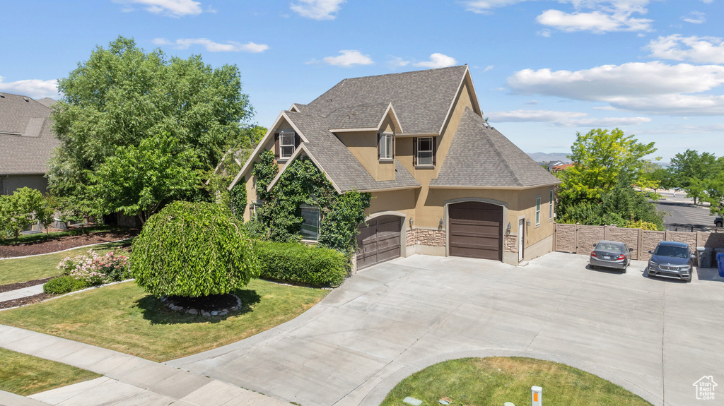 View of front of home with stucco siding, driveway, a shingled roof, stone siding, and a garage