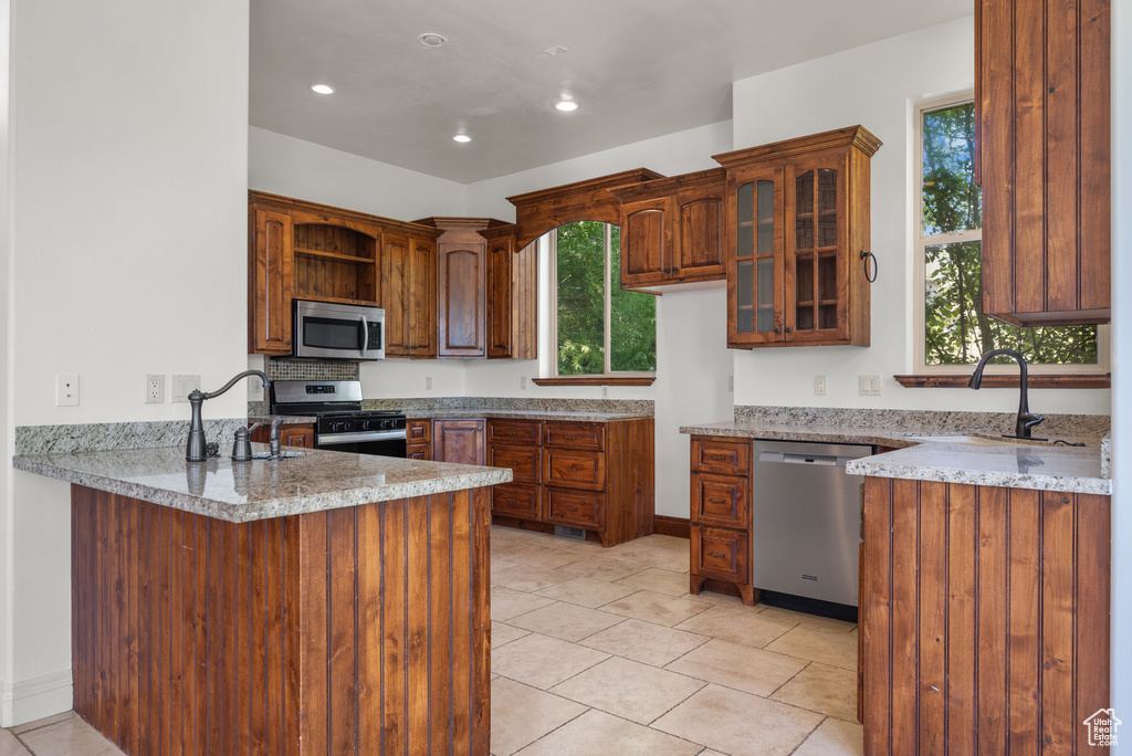 Kitchen featuring appliances with stainless steel finishes, a peninsula, open shelves, glass insert cabinets, and recessed lighting
