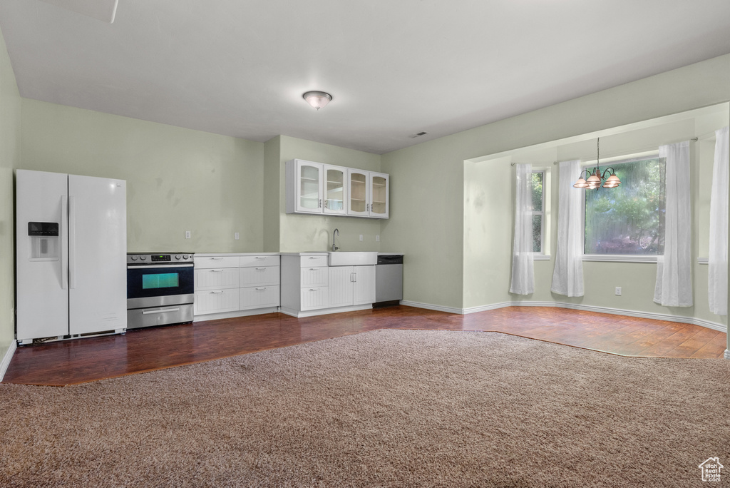 Kitchen featuring stainless steel appliances, dark colored carpet, white cabinets, glass insert cabinets, and a chandelier