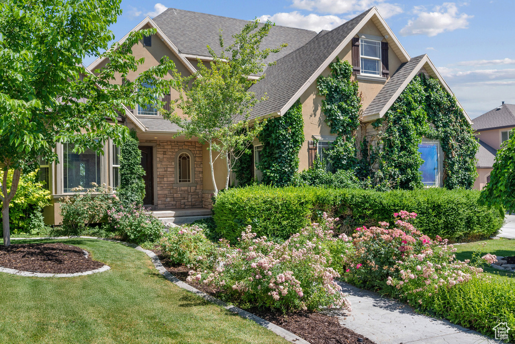 View of front of house featuring stone siding, roof with shingles, a front lawn, and stucco siding