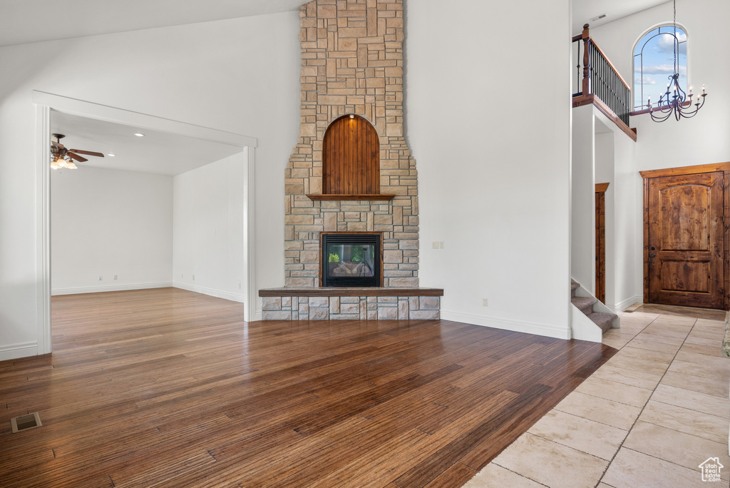 Unfurnished living room with high vaulted ceiling, stairway, a chandelier, wood finished floors, and a stone fireplace