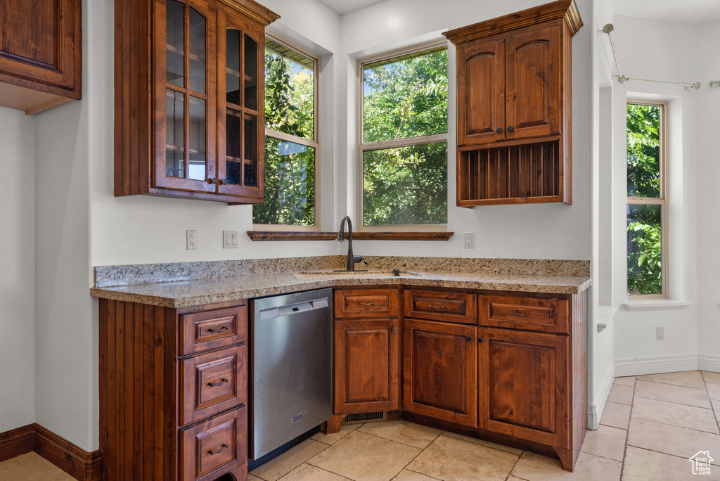 Kitchen with stainless steel dishwasher, light countertops, glass insert cabinets, and light tile patterned floors