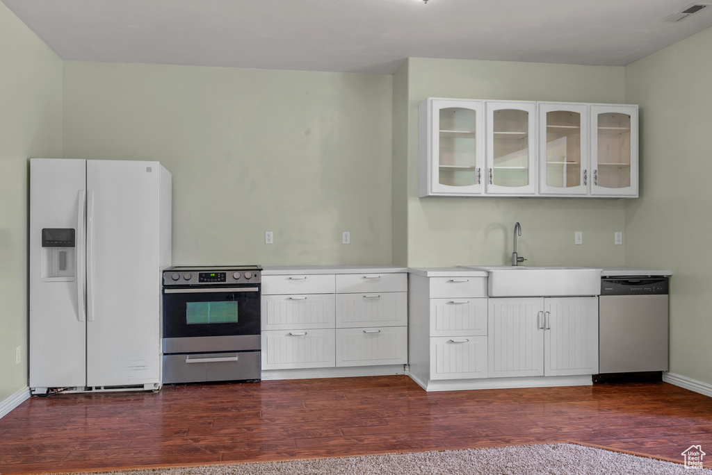 Kitchen with appliances with stainless steel finishes, light countertops, glass insert cabinets, dark wood-type flooring, and white cabinets