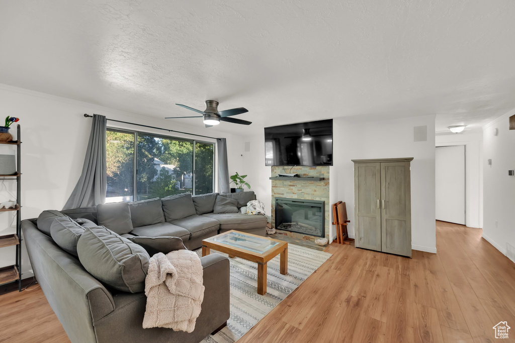 Living area featuring ceiling fan, a stone fireplace, light wood-style floors, and a textured ceiling