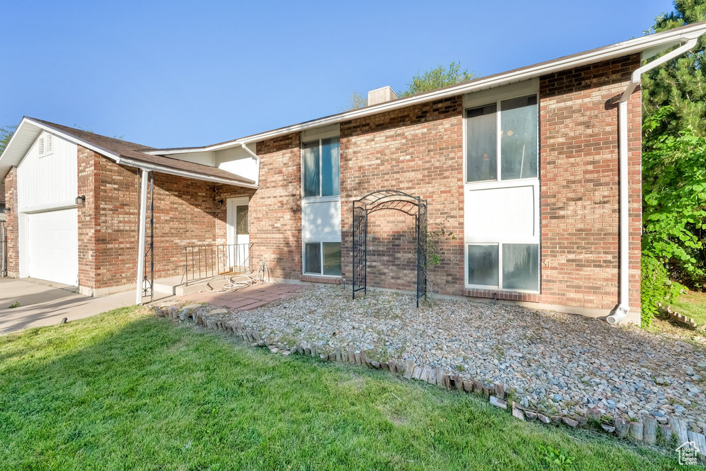 View of front of property featuring a garage, a front lawn, brick siding, driveway, and a chimney