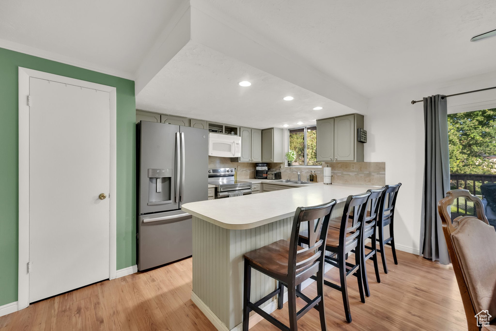 Kitchen featuring stainless steel appliances, a peninsula, light countertops, backsplash, and light wood-style floors