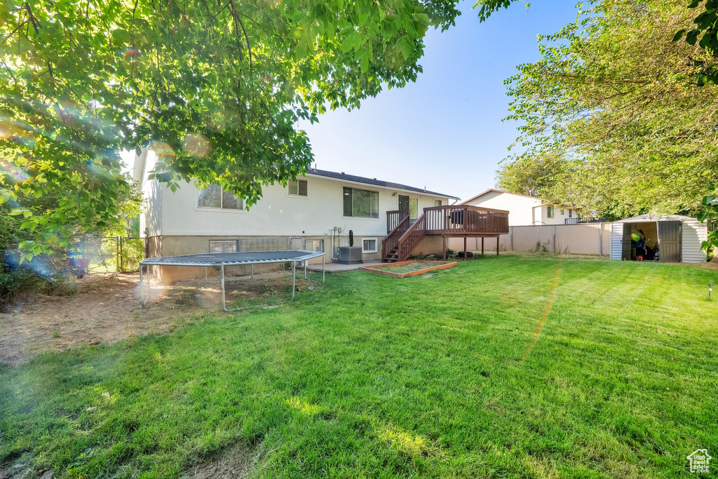 Fenced backyard with a trampoline, a storage unit, a deck, and stairway
