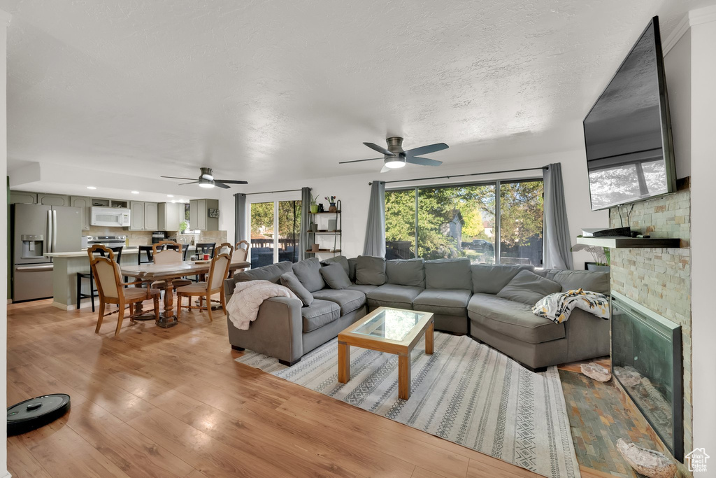 Living room featuring ceiling fan, light wood-style floors, and a glass covered fireplace