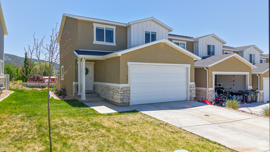 Multi unit property featuring stone siding, board and batten siding, a front yard, stucco siding, and concrete driveway