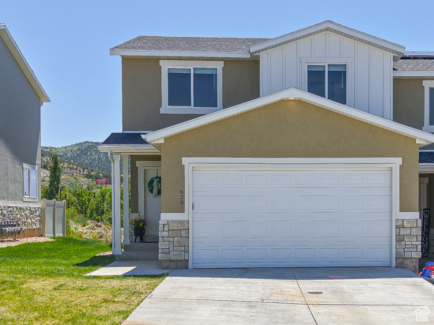 View of front facade featuring stone siding, concrete driveway, a front lawn, and roof mounted solar panels