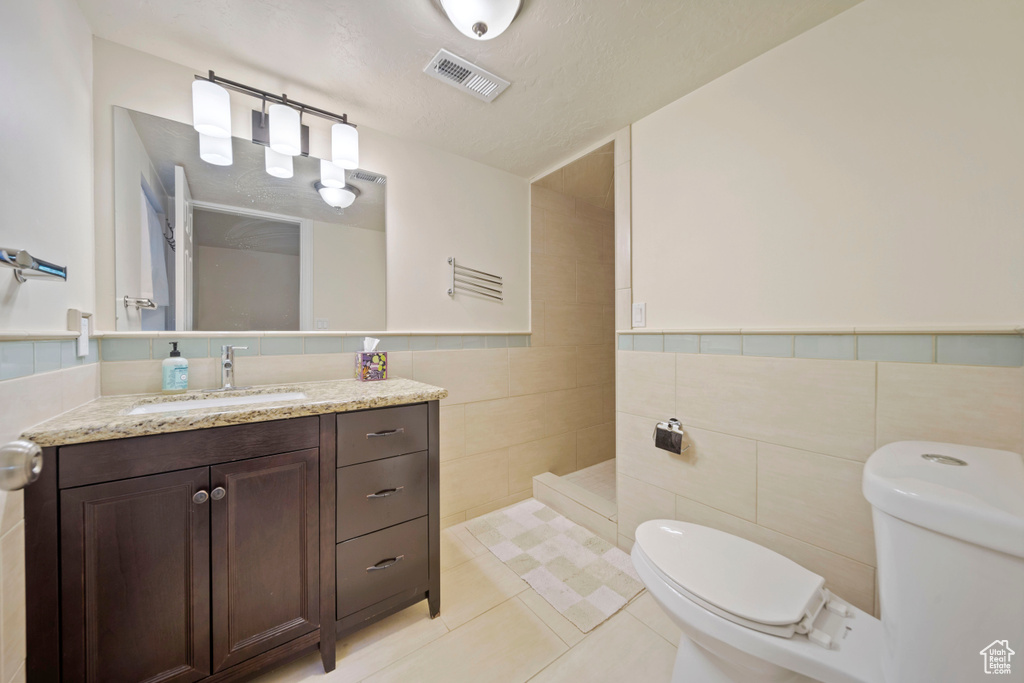 Full bathroom featuring tile walls, vanity, tile patterned floors, a walk in shower, and a wainscoted wall