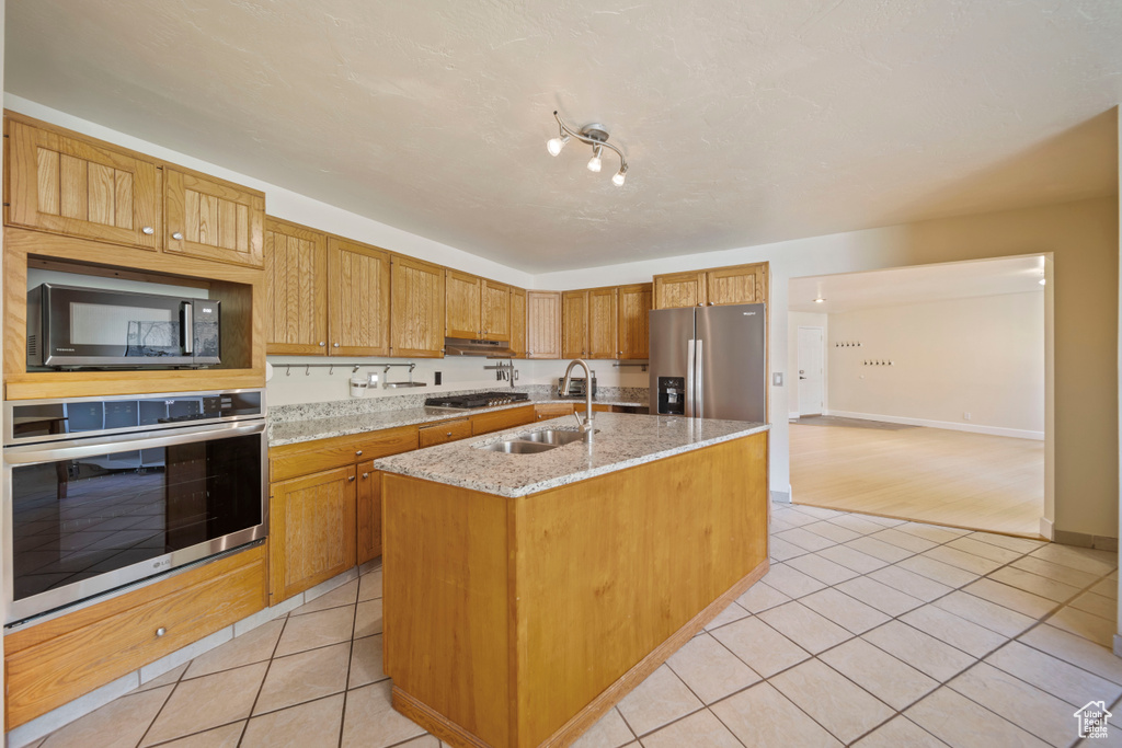Kitchen with stainless steel appliances, light tile patterned flooring, a kitchen island with sink, light stone counters, and under cabinet range hood
