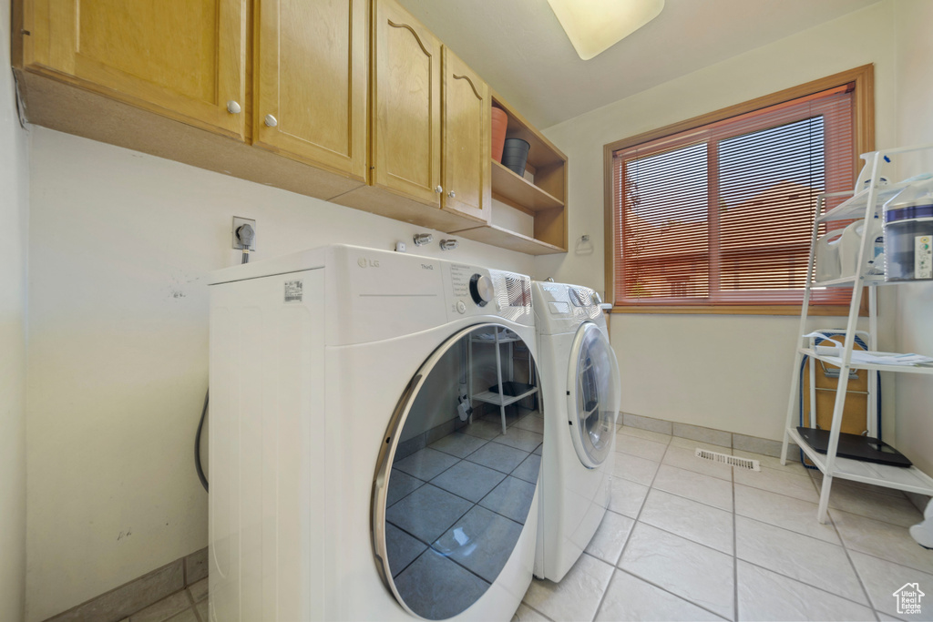 Washroom featuring cabinet space, washing machine and clothes dryer, and light tile patterned floors
