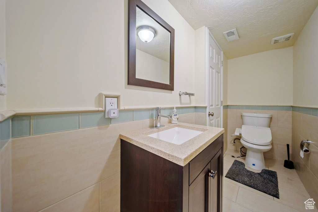 Half bath with tile patterned floors, vanity, a textured ceiling, wainscoting, and tile walls