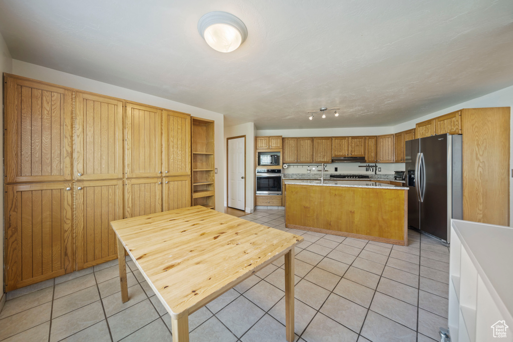 Kitchen with appliances with stainless steel finishes, light tile patterned flooring, light countertops, a kitchen island with sink, and under cabinet range hood