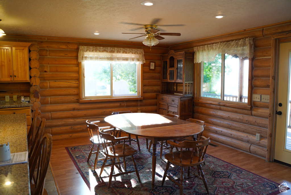 Dining area featuring a ceiling fan, plenty of natural light, wood finished floors, log walls, and recessed lighting